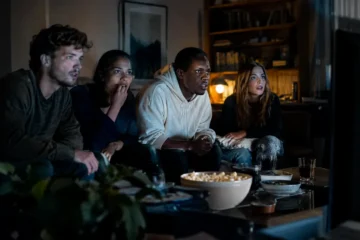 streaming service consolidations shown through viewers choosing films on a couch